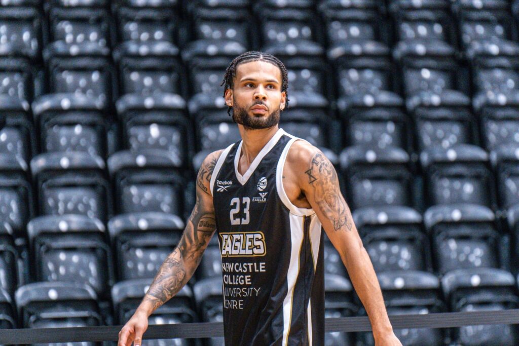 Player Jordan Spencer stands in the arena. The picture is framed from his waist up, he is standing in front of the arena seats with his arms by his sides.