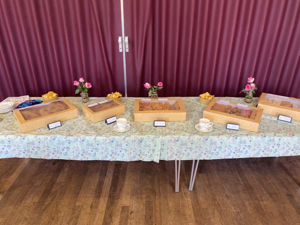Two tables dressed with a floral tablecloth display boxes of afternoon tea treats.